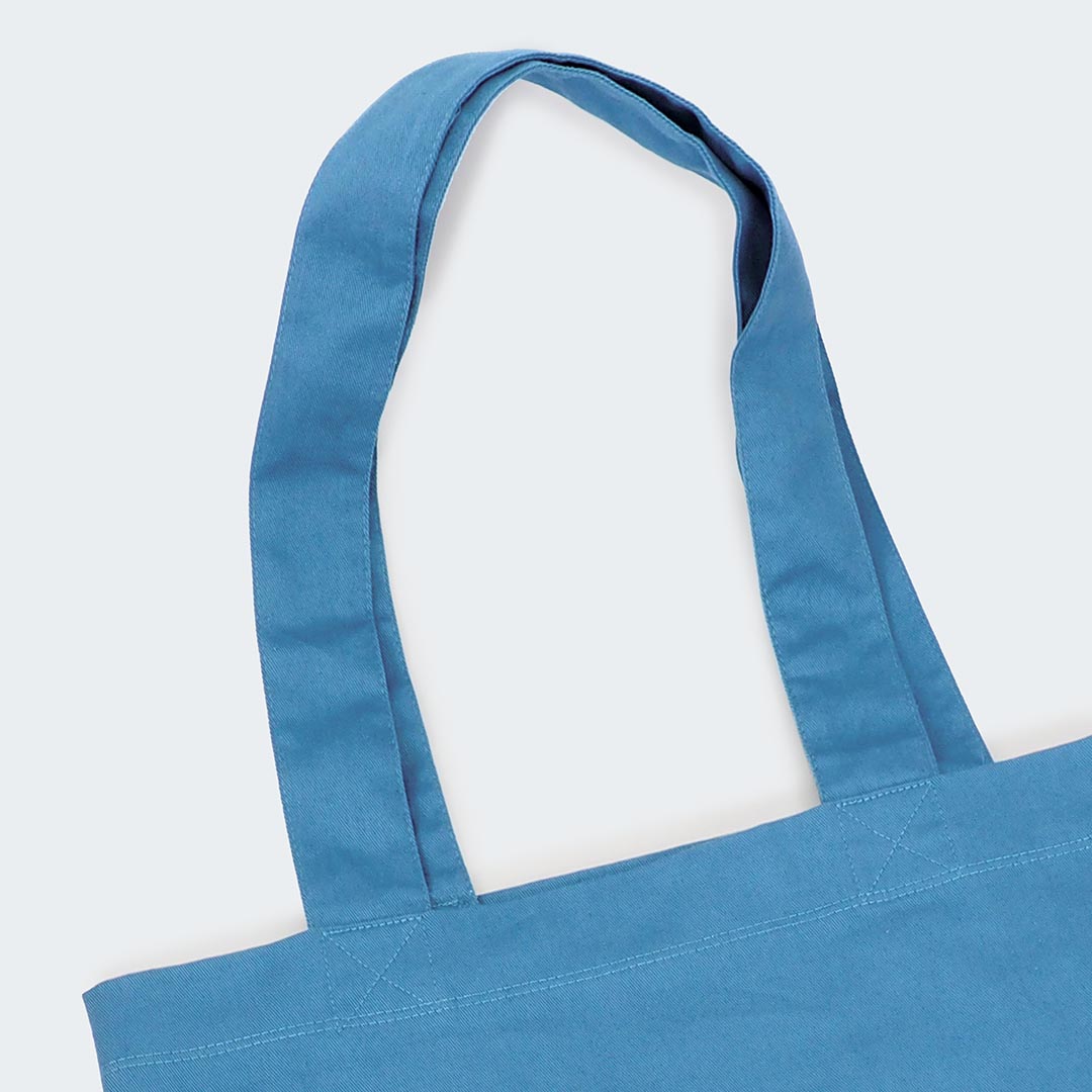 Das Bild zeigt die langen Henkel der hellblauen Stofftasche. Die Henkel sind so lang, dass die Tasche bequem über der Schulter getragen werden kann.